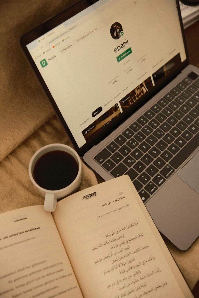 A serene workspace setup with a laptop, open book in Arabic, and a cup of coffee.